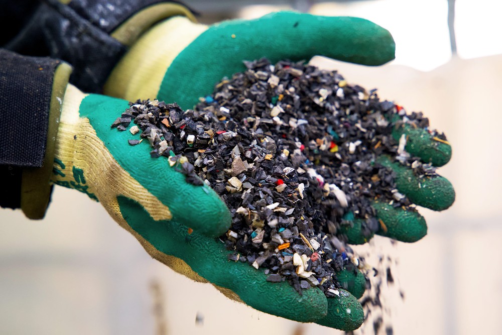 Reziduri de plastic în vederea reciclării, ținute în mănuși de cauciuc.
