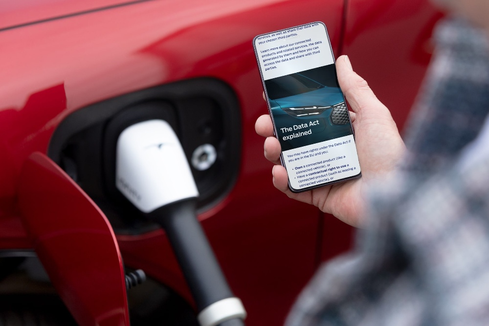 O persoană care citește un document explicativ legat de Actul UE privind datele pe telefonul său lângă un vehicul electric care se încarcă.