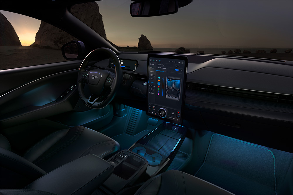 Interiorul unui Ford Mustang Mach-E pe timp de noapte, cu ecranul tactil SYNC 4 de 15,5" și iluminarea ambientală cu LED-uri setată pe culoarea albastru.