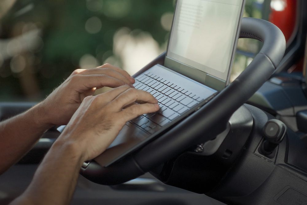 Mâinile unei persoane tastează pe un laptop așezat pe volanul rabatabil al Ford Tourneo Custom