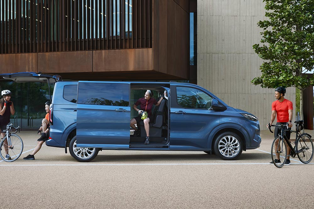 Ford Tourneo Custom culoare albastră parcată cu ușile laterale deschise și oameni cu biciclete în apropiere