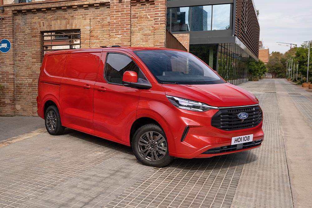 Ford Transit Custom roșu parcat langă o clădire.