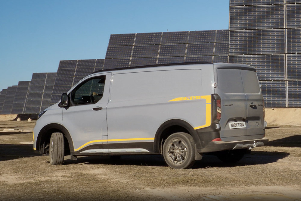 Un Ford Transit Custom Trail Van griu cu accente galbene parcat în fața unor panouri solare.