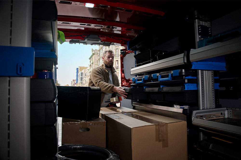 O persoană care pune un colet în interiorul unui Ford Transit Custom roșu.