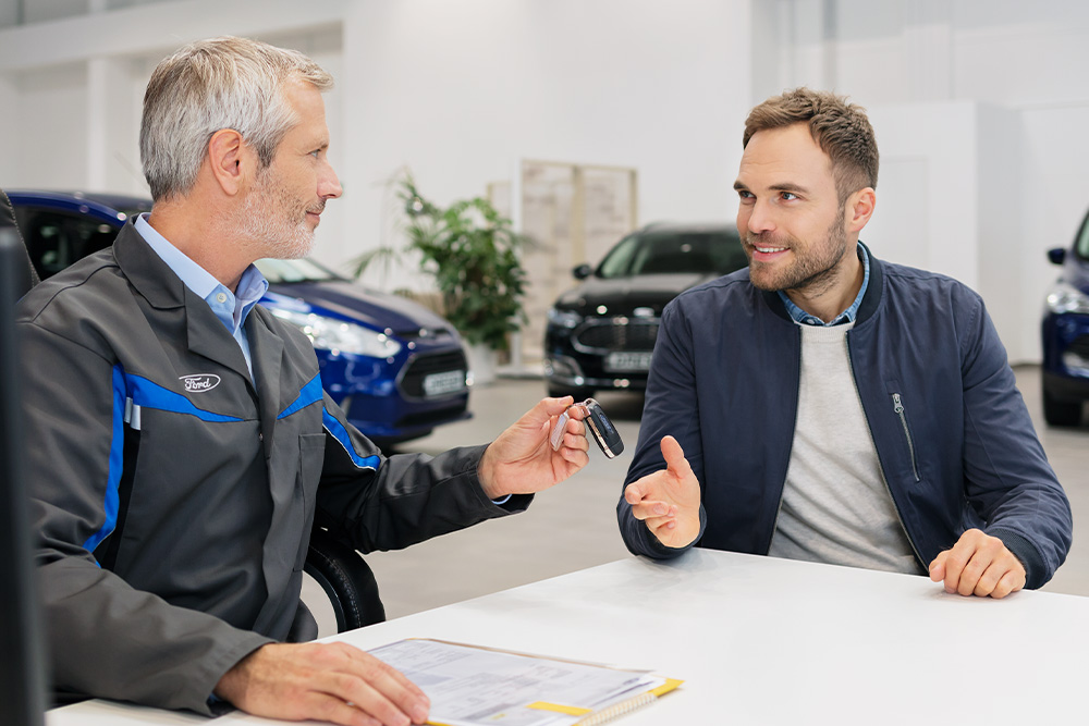 Consultantul Ford înmânează cheile clientului în timp ce discută despre gama de opțiuni de finanțare Ford.