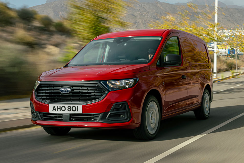 Un Ford Transit Connect deplasându-se pe șosea, prezentând grila față și farurile automate.