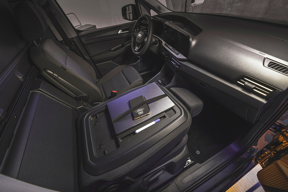 Interiorul unui Ford Transit Connect prezentând tabloul de bord, scaunele, volanul, un laptop și un telefon pe consola centrală.