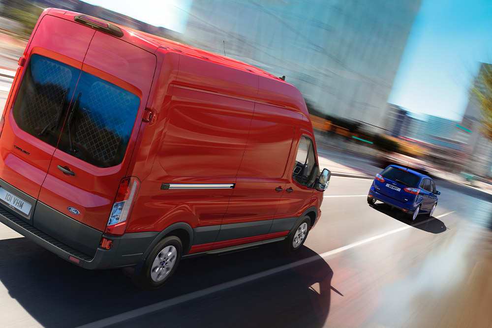 Furgonetă Ford Transit roșie circulând pe șosea.
