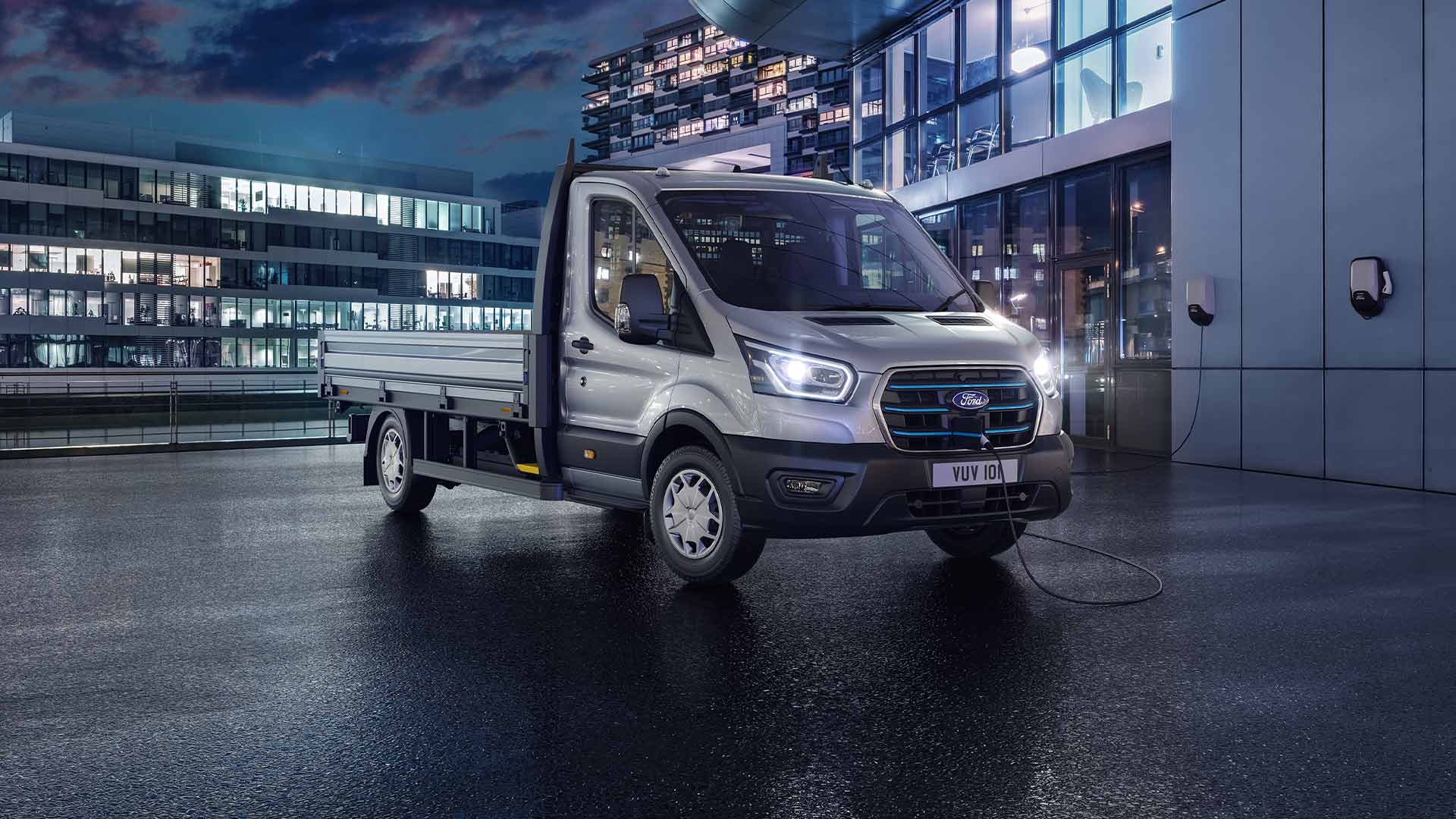 Transit Autoșasiu cu Simplă Cabină, culoare Moondust Silver  parcat în fața unei clădiri moderne pe timp de noapte.